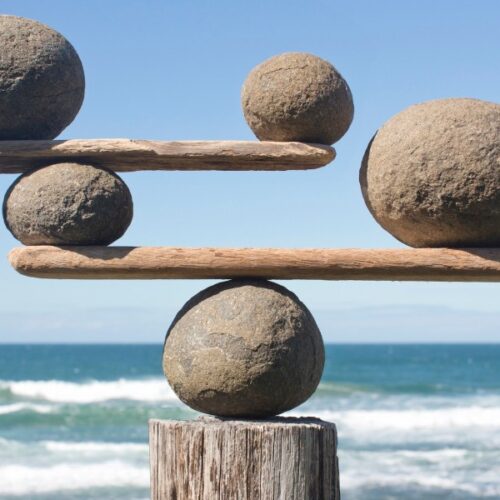 A balance structure made of rocks and wood against a seaside background