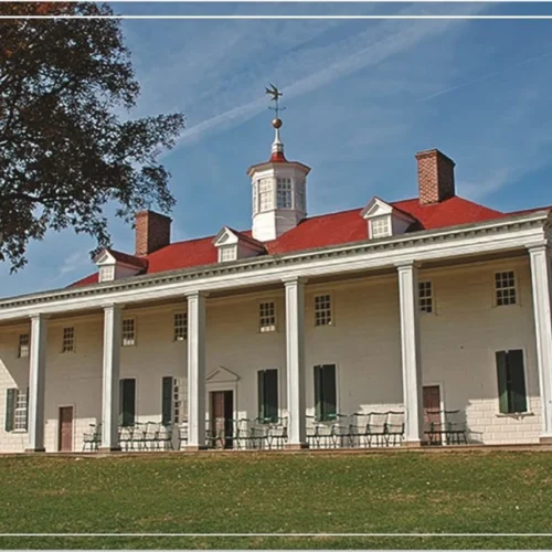A large historical mansion with a red roof and white pillars surrounded by trees.