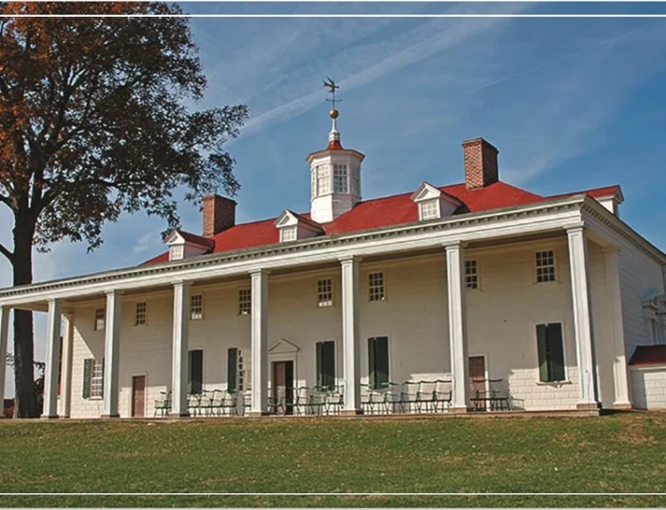 A large historical mansion with a red roof and white pillars surrounded by trees.