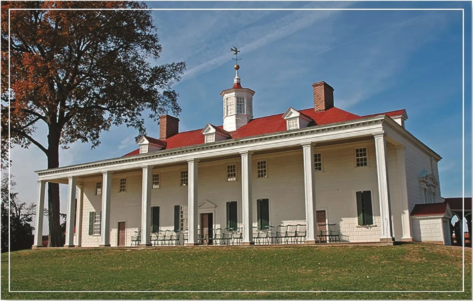 A large historical mansion with a red roof and white pillars surrounded by trees.